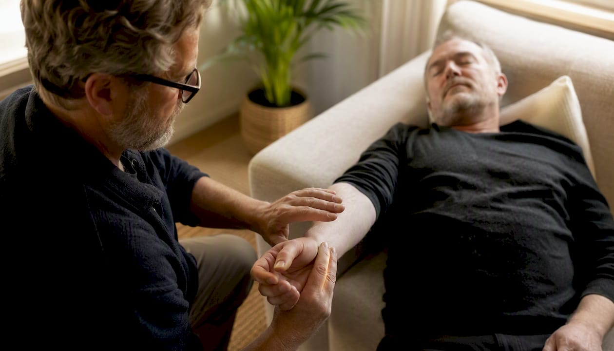 Ein Hypnotiseur führt eine Mesmerismus-Sitzung durch und streicht dabei sanft über den Arm des Klienten.