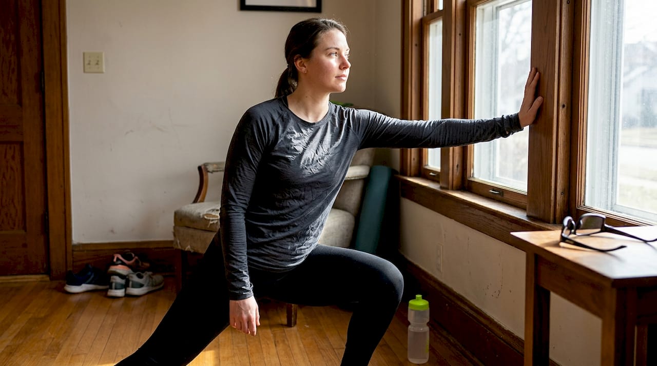 Cyclist stretching by sunny window with water bottle