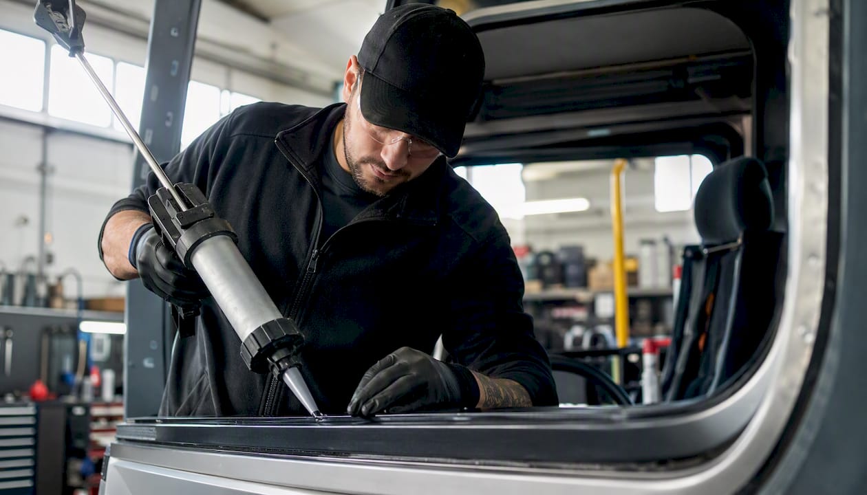 Technician applying adhesive to truck windshield frame