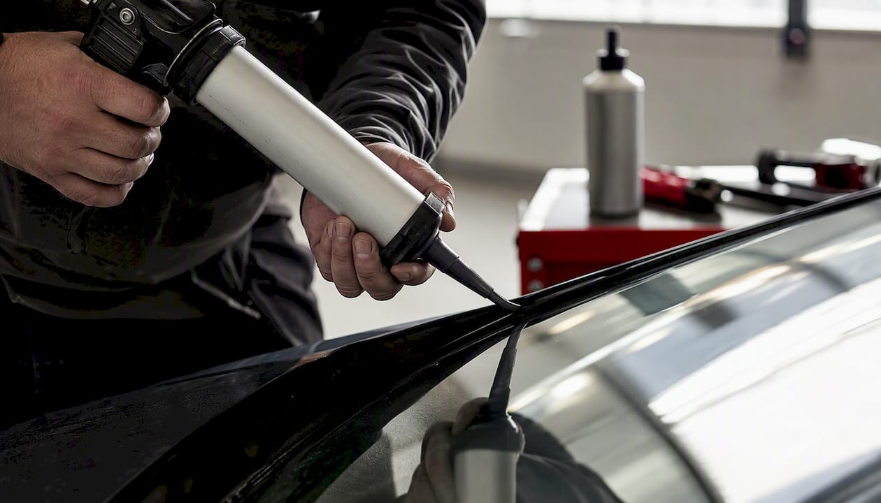 Technician applying urethane adhesive to windshield frame edge