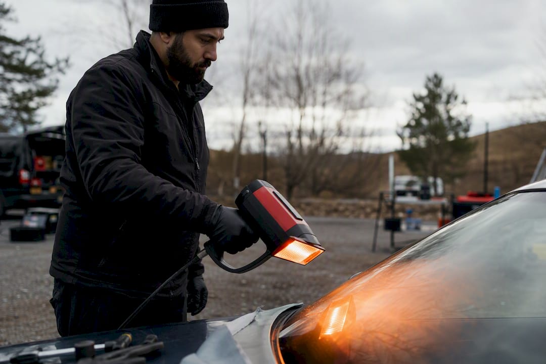Technician warming windshield glass with portable heater
