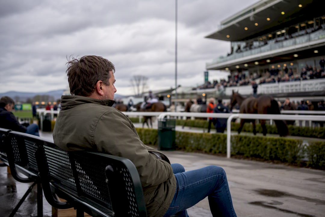 Bettor pausing alone at racetrack bench