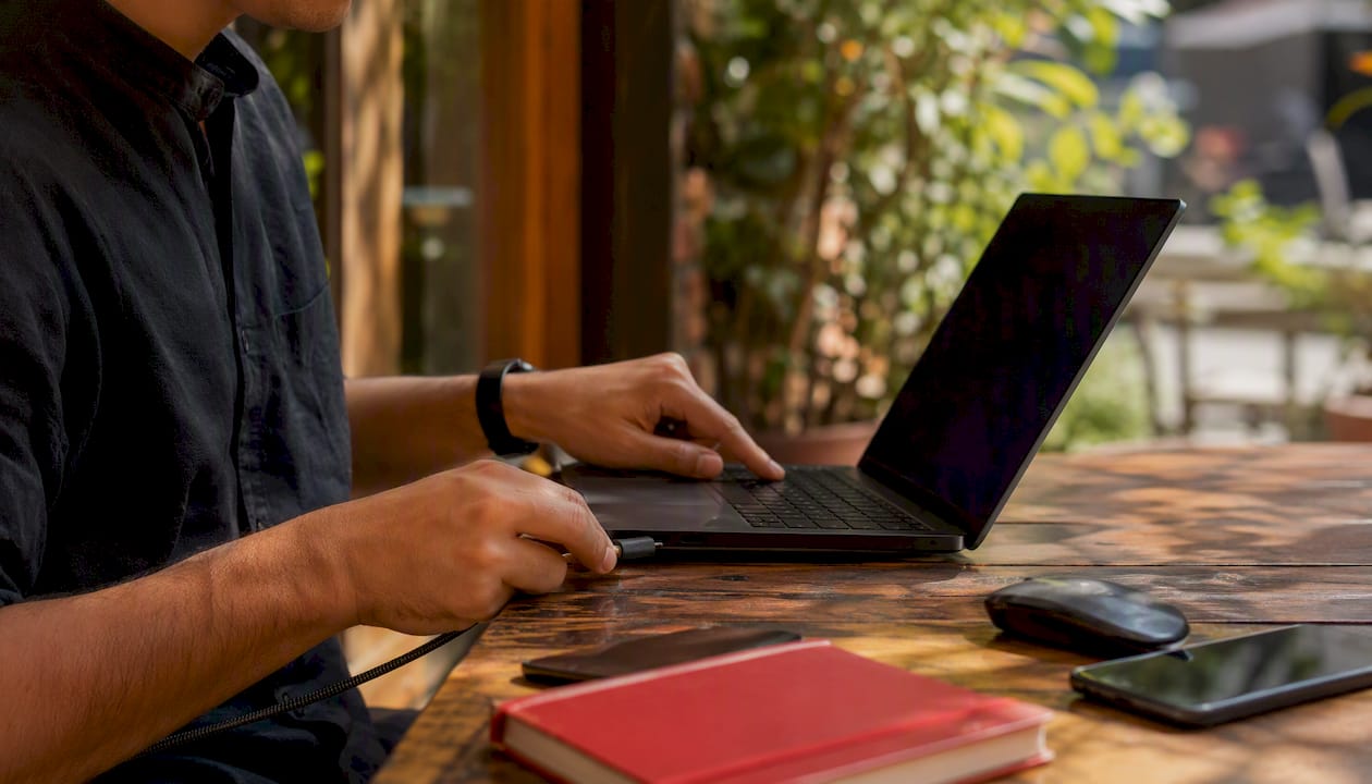 Hands plugging charger into laptop in workspace