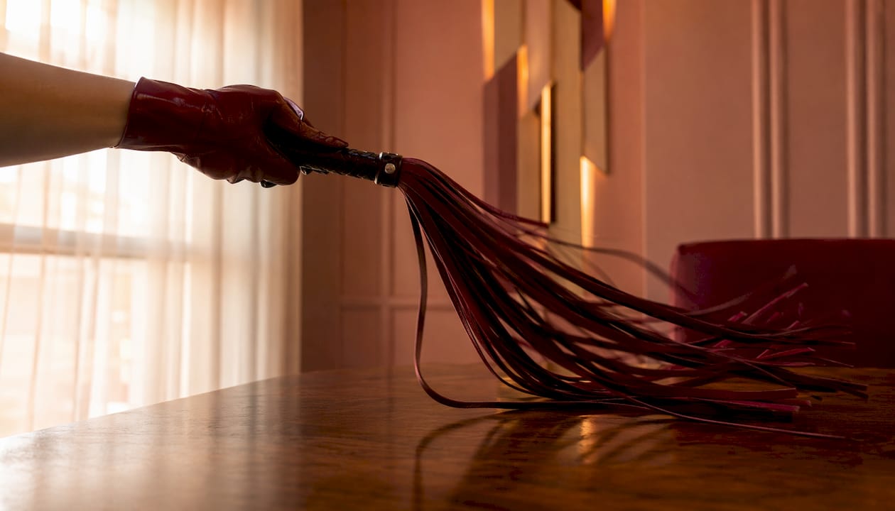 Gloved hand swinging suede flogger tails