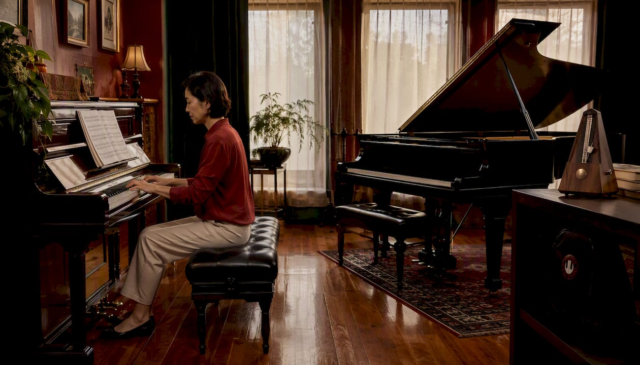 Woman sitting by grand and upright pianos in showroom