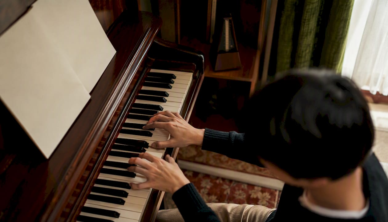 Hands playing piano keys with metronome nearby