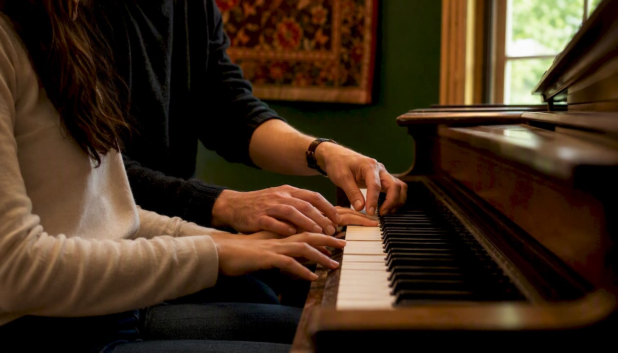 Teacher guiding student hands on piano keys