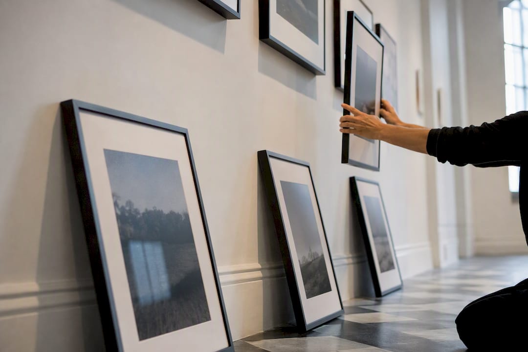 Hands hanging framed photo prints in gallery