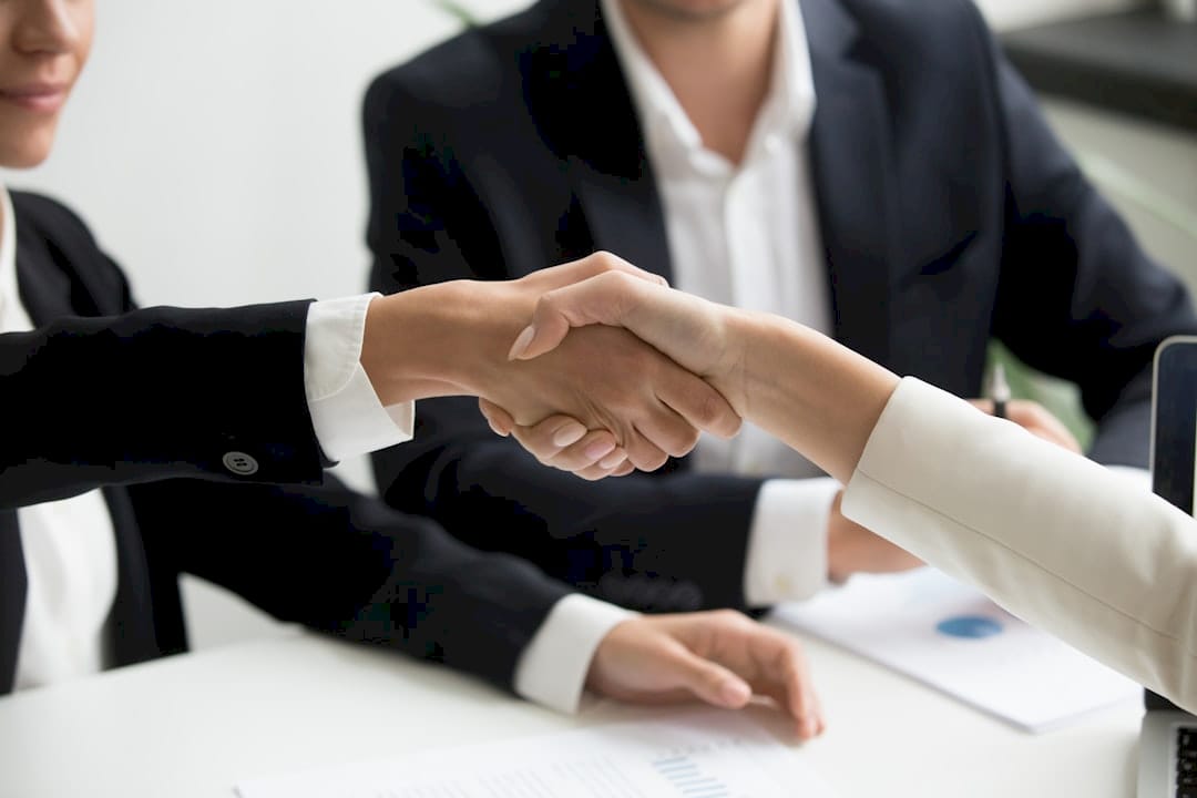 two people shaking hands in front of a laptop