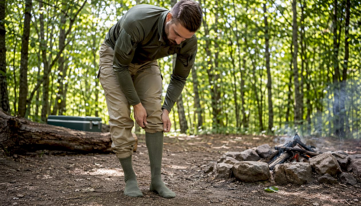 Close-up hands folding tactical pants into socks outdoors