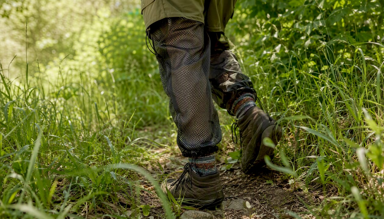 Hiker's legs in mesh over-pants stepping through tall grass
