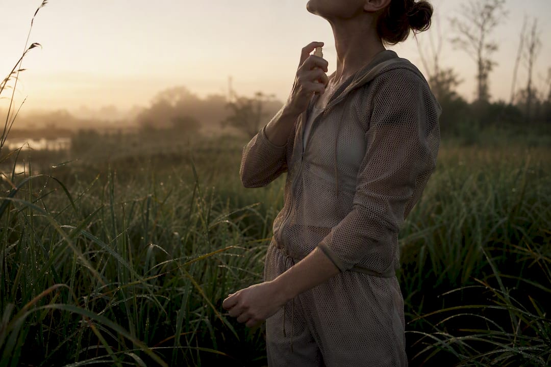 Person in mesh clothing applying repellent in marsh at dawn