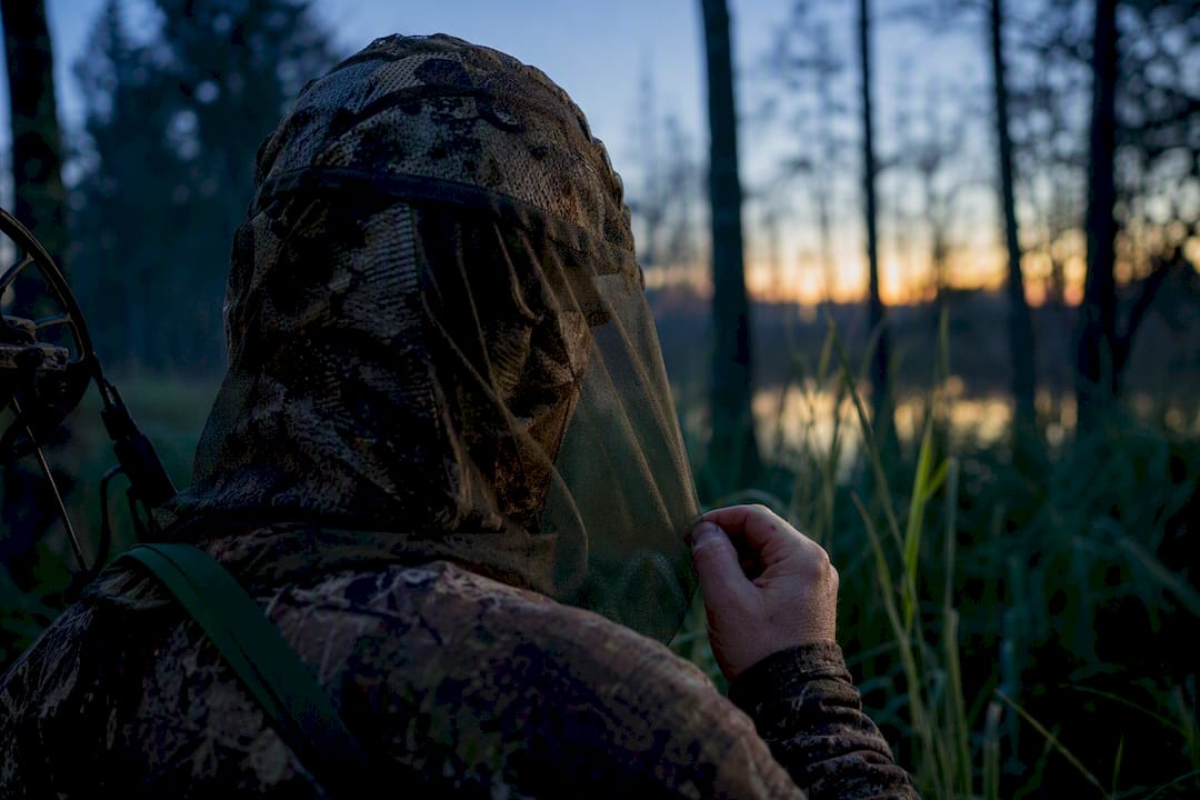 Bowhunter adjusting mesh protection in forest