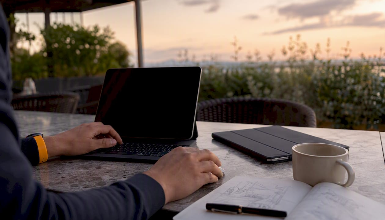 Im Coworking-Space arbeiten Hände gleichzeitig am Laptop und Tablet.