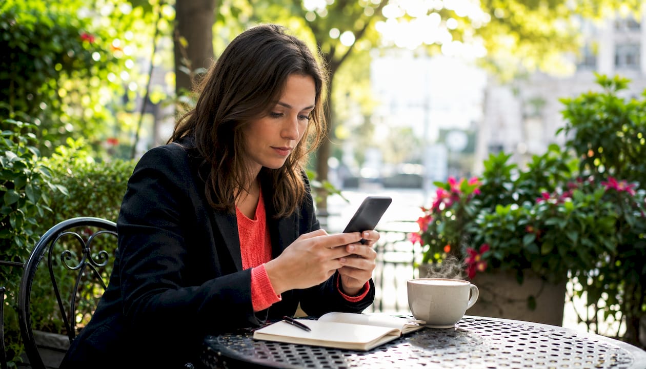 Une femme consulte son téléphone portable attablée dans un café
