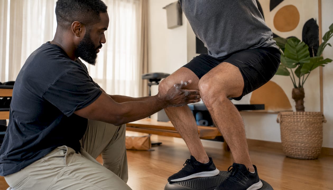 Therapist guiding knee alignment during mini-squat exercise