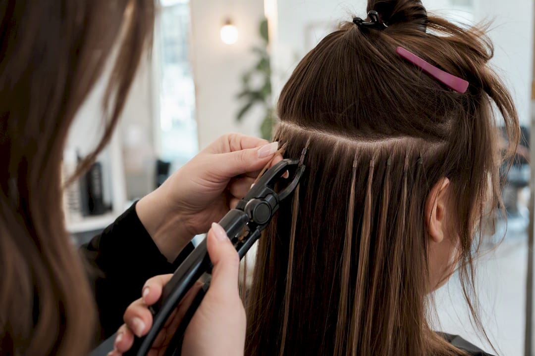 Stylist installing i-tip hair extension with bead