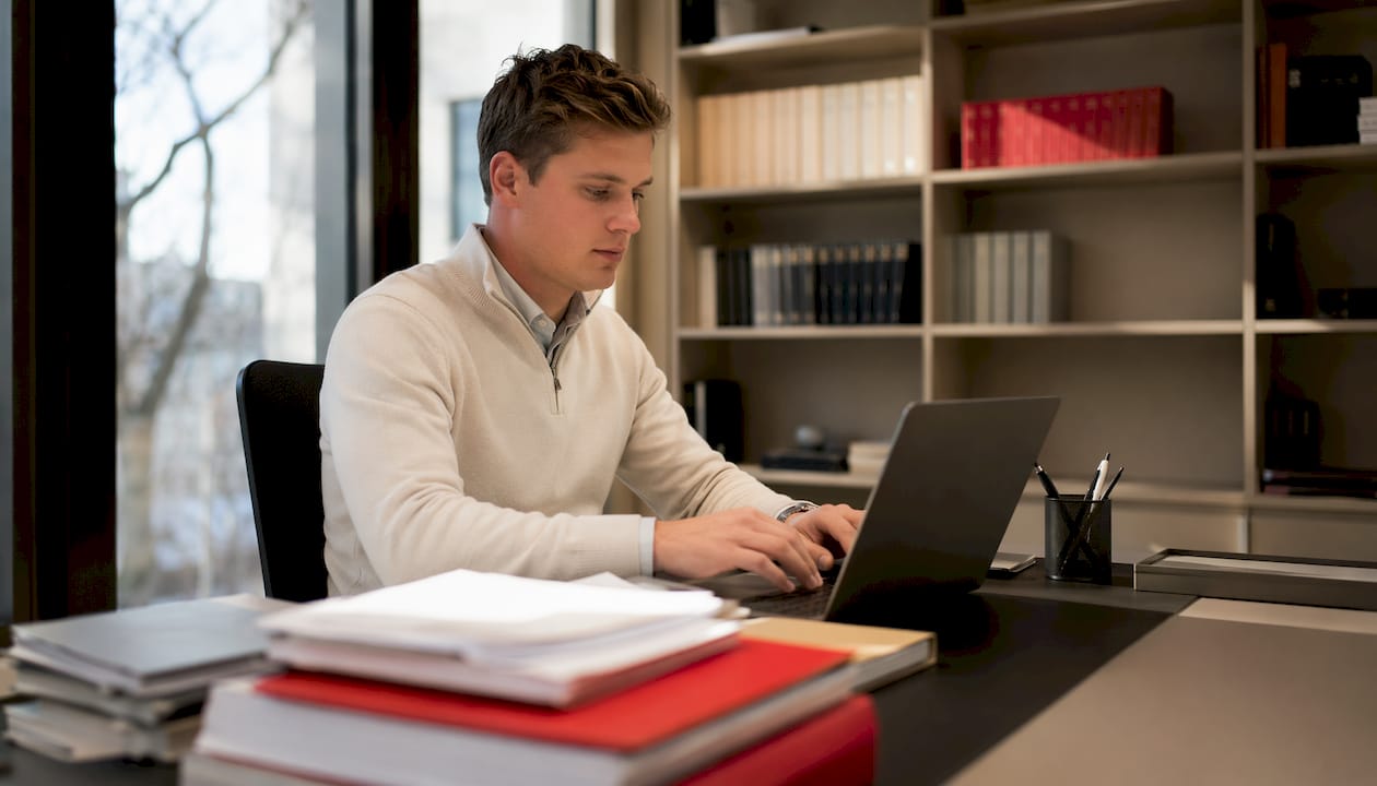 Detailansicht: Jemand arbeitet am Laptop, daneben liegen Schweizer Rechtsdokumente.