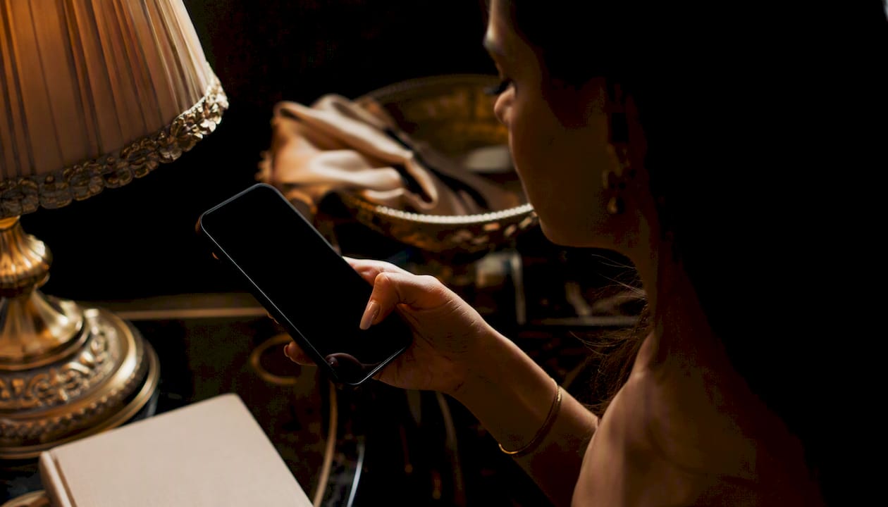 Hand unlocking iPhone with Face ID in warm dark room