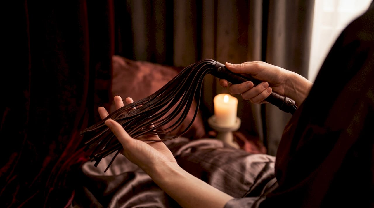 Hands holding flogger swinging in intimate room