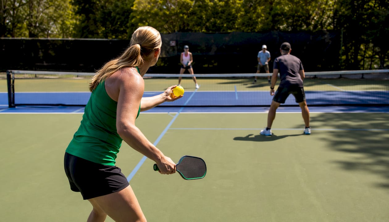Mixed doubles pickleball players serving and waiting
