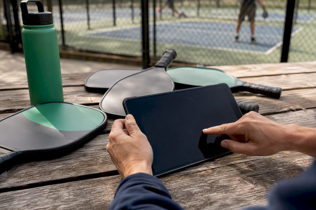 Hands pressing refund on tablet near pickleball gear