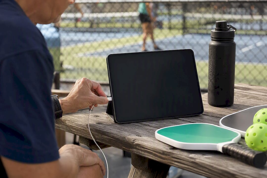 Hand plugging charging cable into tablet at pickleball table