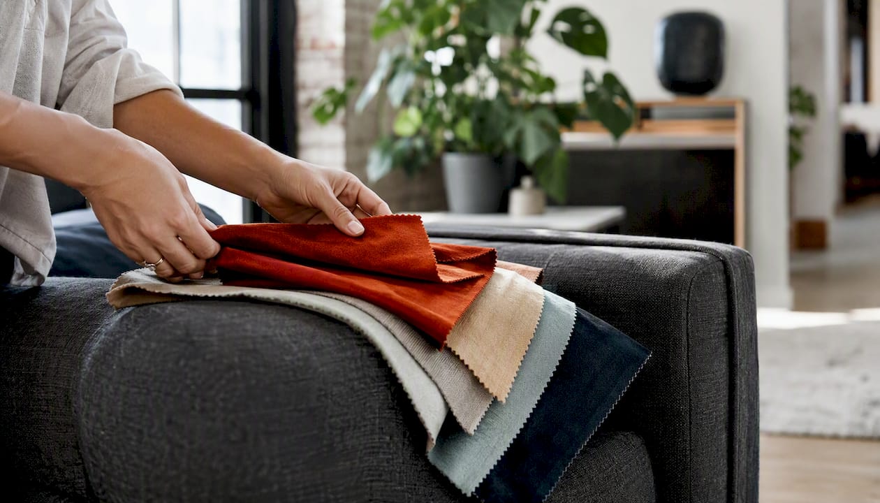 Hands holding sofa fabric swatches on sofa