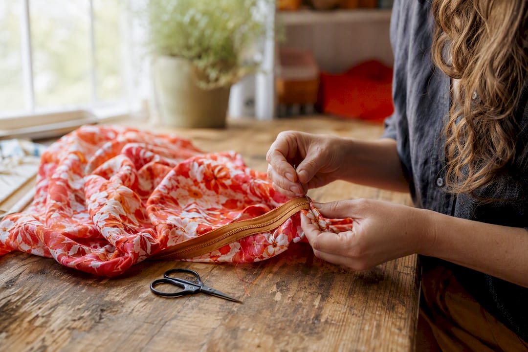 Hands sewing zipper onto fabric