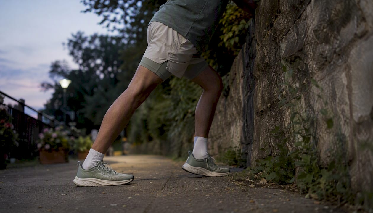 Runner stretching calf muscles outdoors at sunset