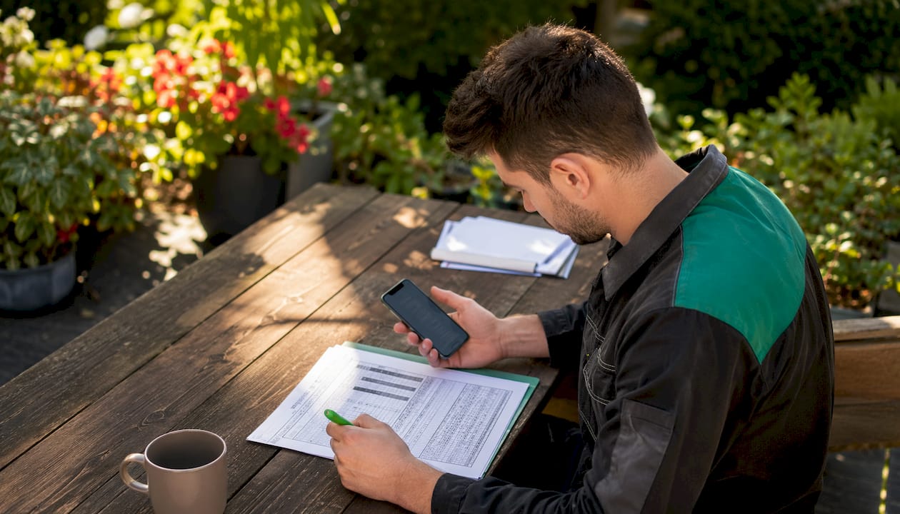Ein Techniker sitzt am Tisch, blickt auf sein Smartphone und prüft seinen aktuellen Schichtplan.