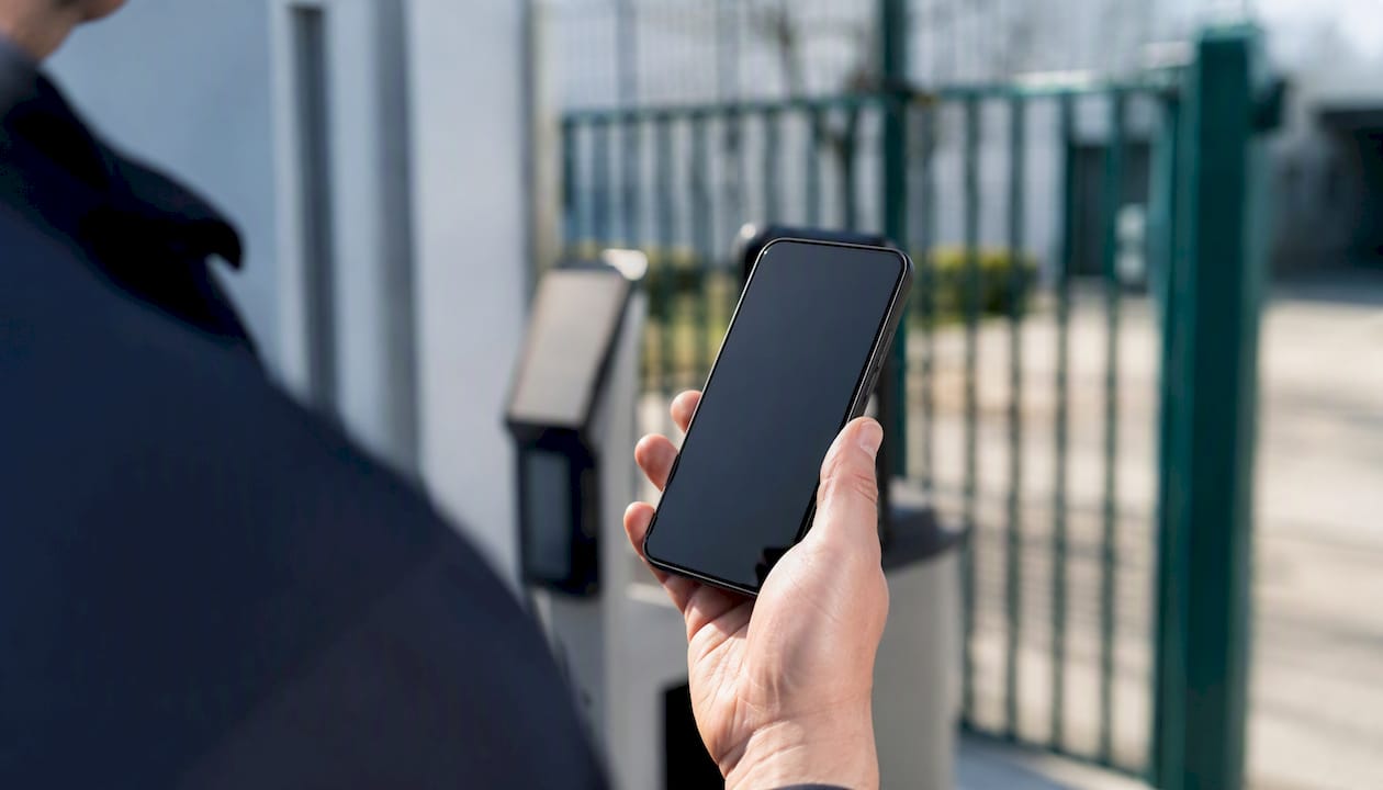 Ein Sicherheitsmitarbeiter steht draußen und hält sein Smartphone in der Hand, dessen Display ausgeschaltet ist.