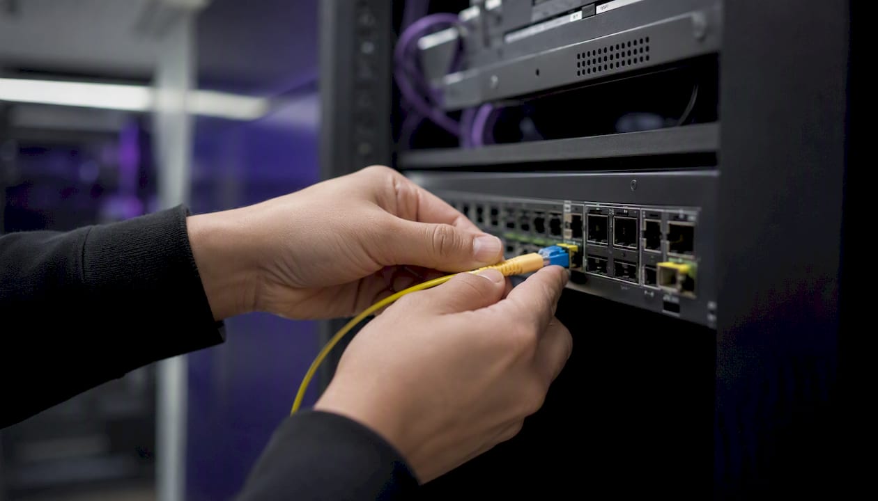 Hands connecting fiber optic cable to network switch