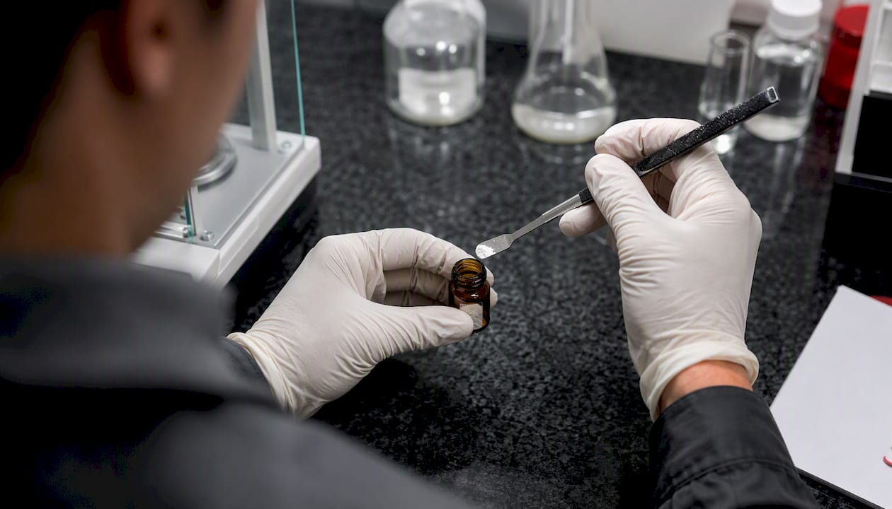 Hands transferring 7-hydroxymitragynine powder into amber vial