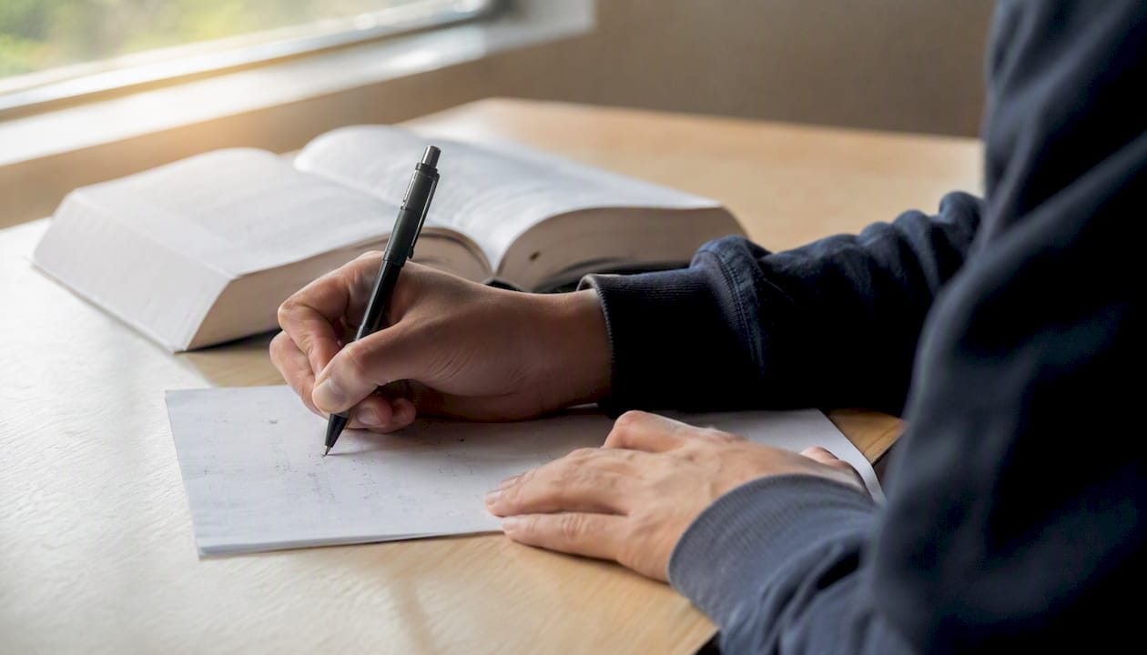 Student writing on exam sheet in test hall