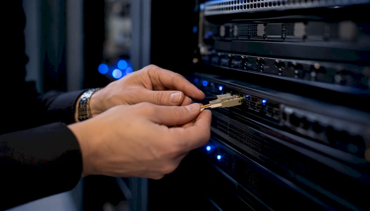 Hands connecting fiber optic cable in server rack