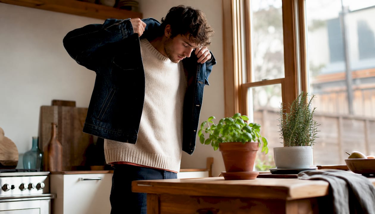 Man layering denim jacket indoors in natural light