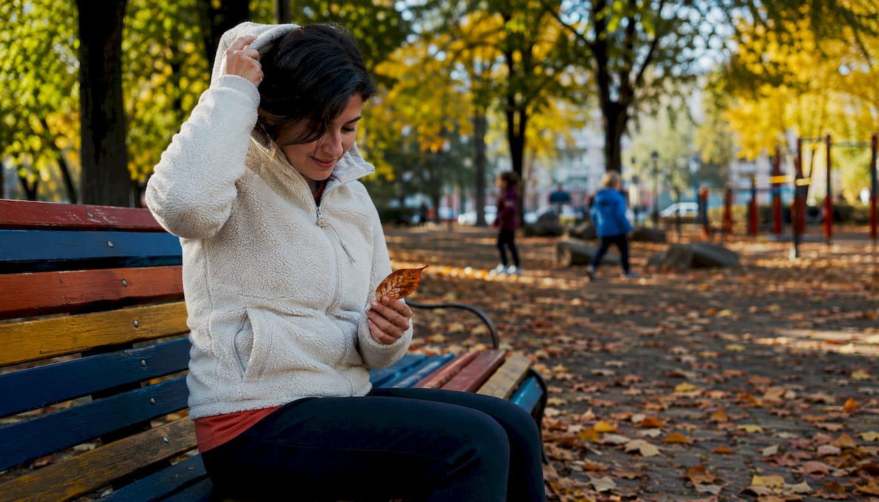 Woman layering fleece hoodie outdoors on bench