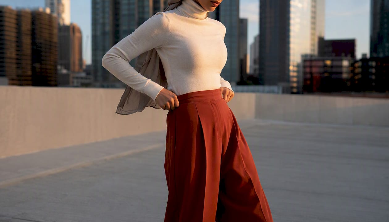 Person adjusting wide-leg trousers and fitted turtleneck