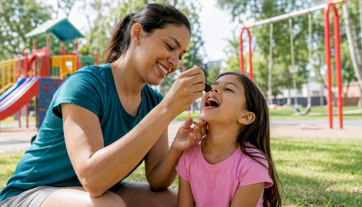Mother giving daughter vitamin D drops in park