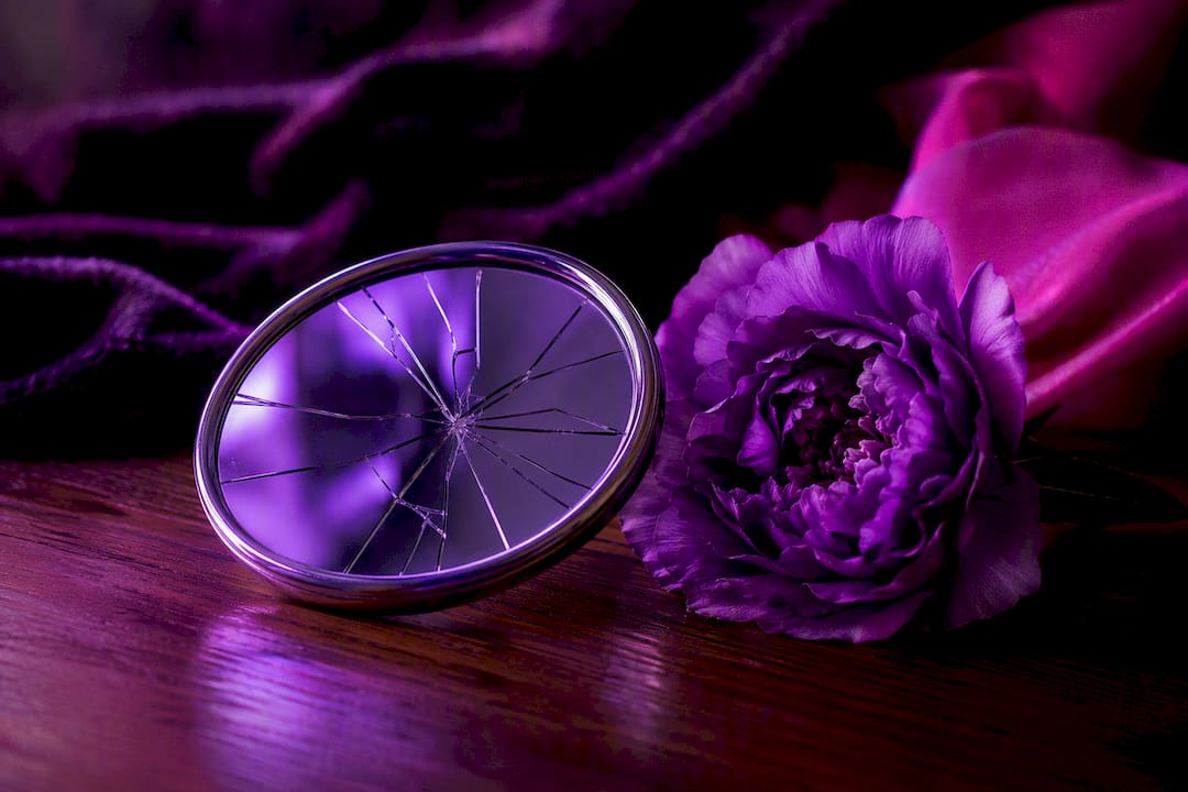 Cracked mirror and blooming flower on table