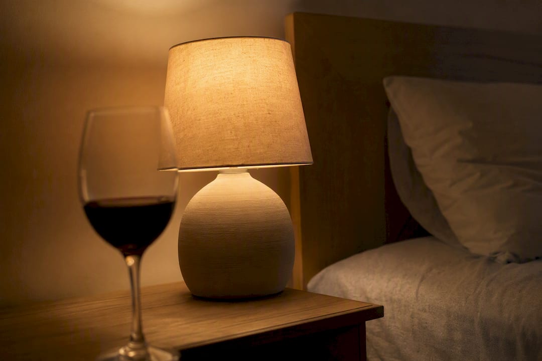 Copa de vino y luz cálida de lámpara sobre la mesita de noche
