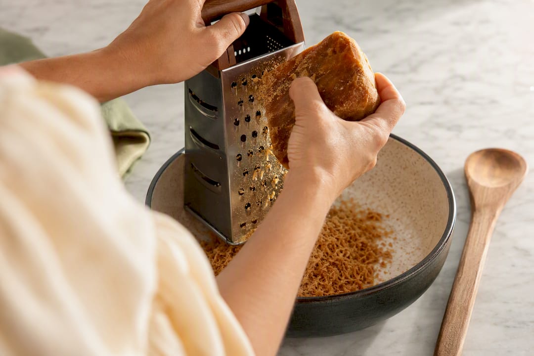 Hands grating panela into ceramic bowl