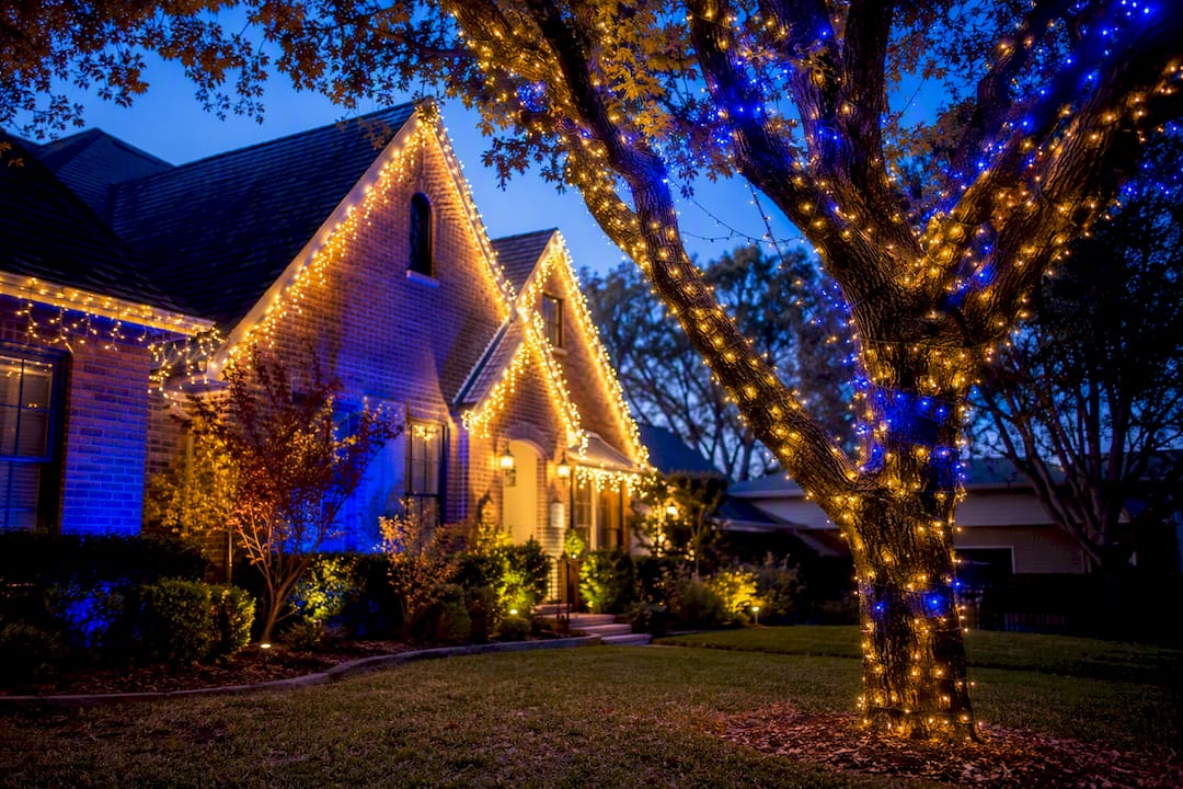 Blue and gold holiday lights on brick house and tree