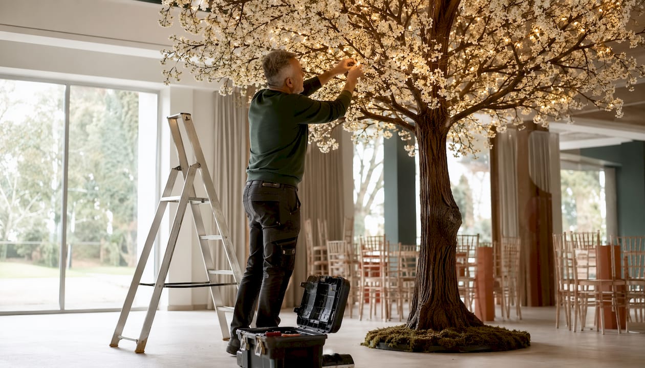 Ein Dekorateur bringt Lichter am künstlichen Baum an.