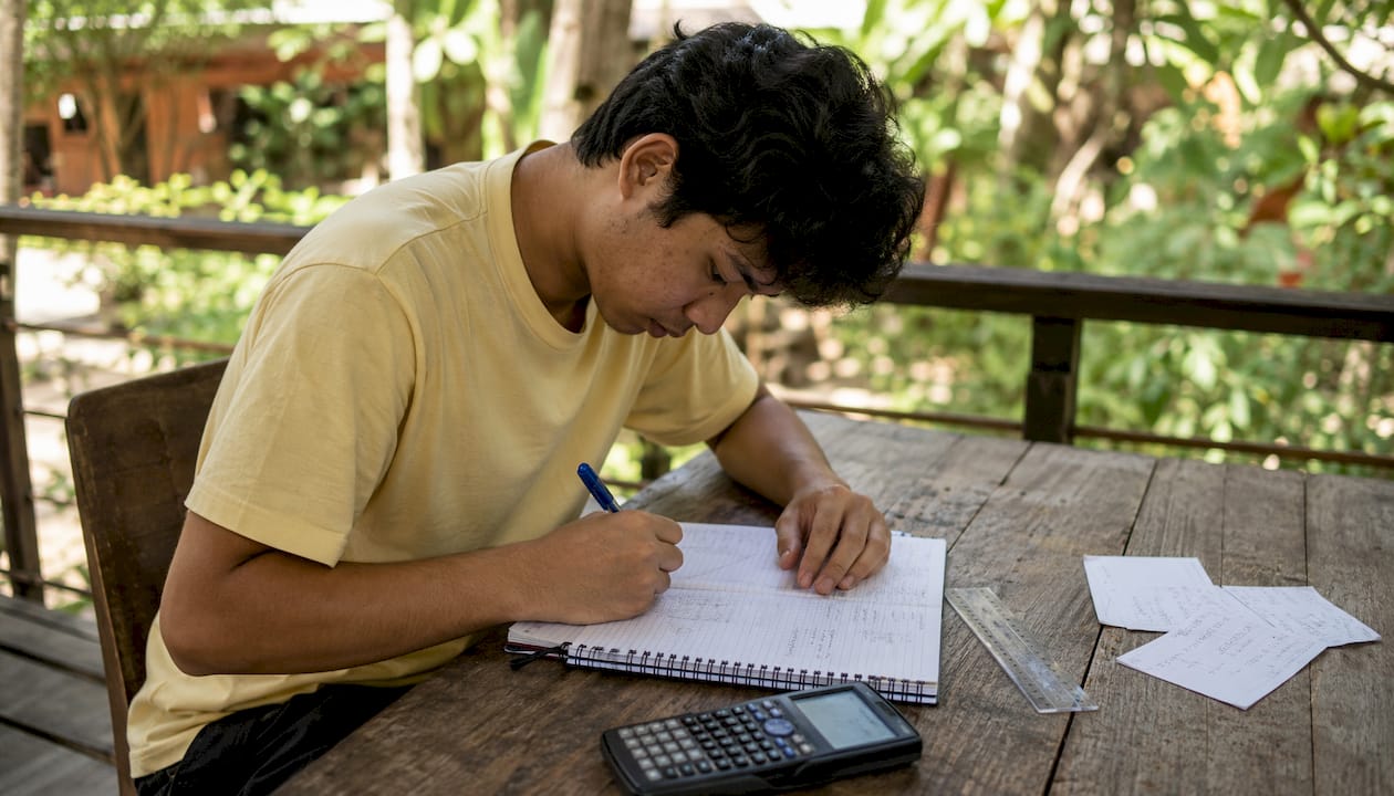 Hands writing maths problems with calculator nearby