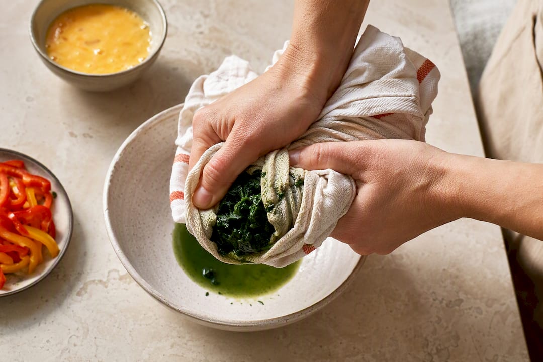 Hands squeezing moisture from spinach