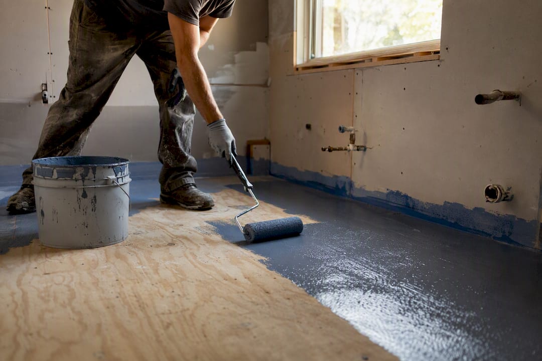 Hands applying waterproof membrane to plywood floor