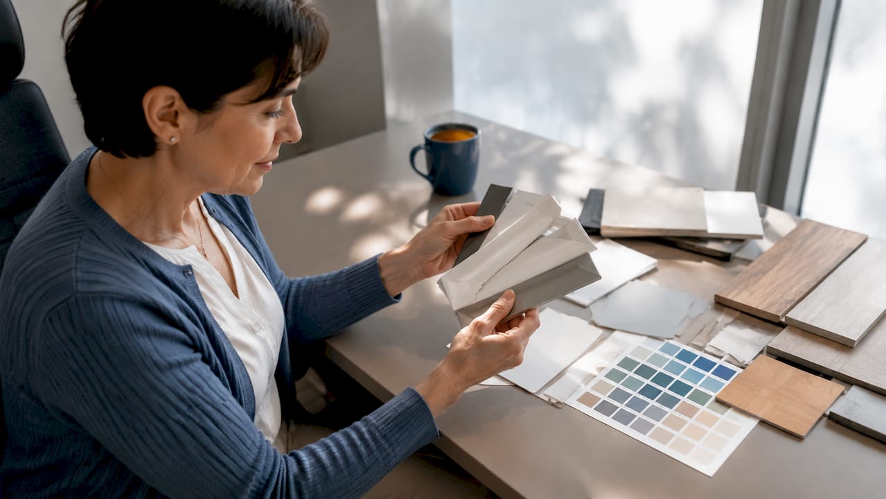 Een vrouw bekijkt verschillende witte kleurstalen voor kozijnen in huis.