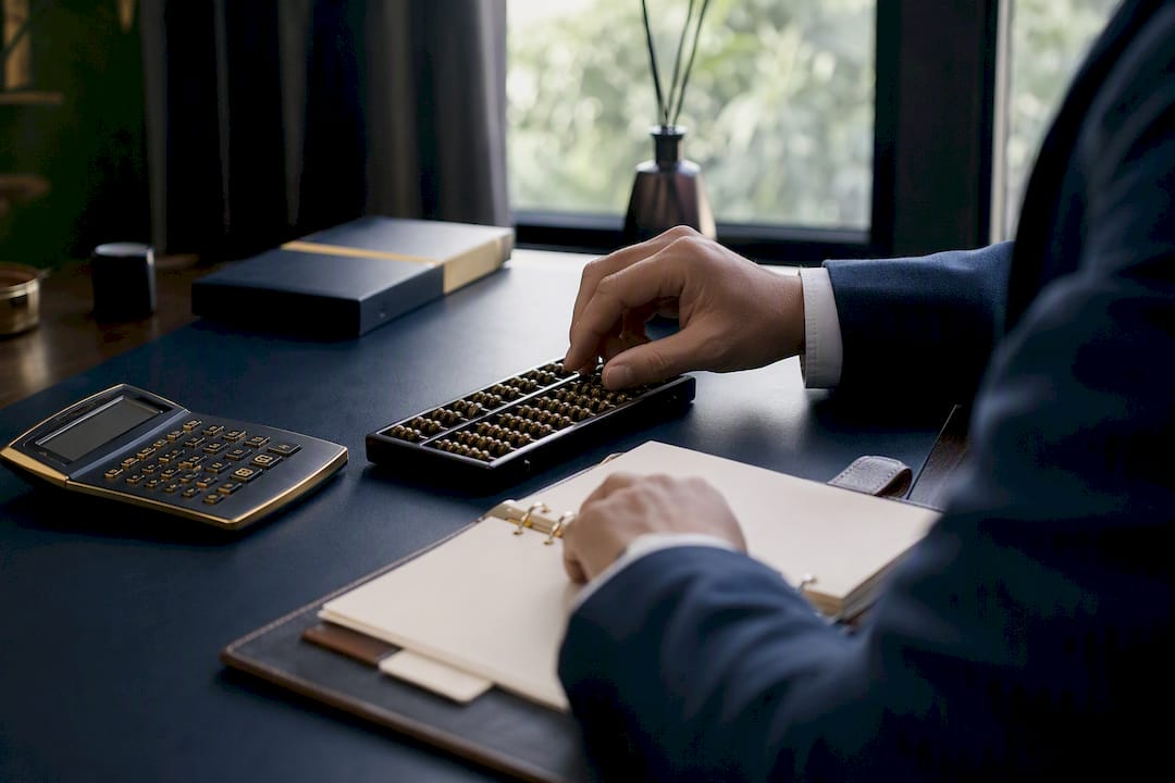 Hand adjusting abacus amidst calculator and planner
